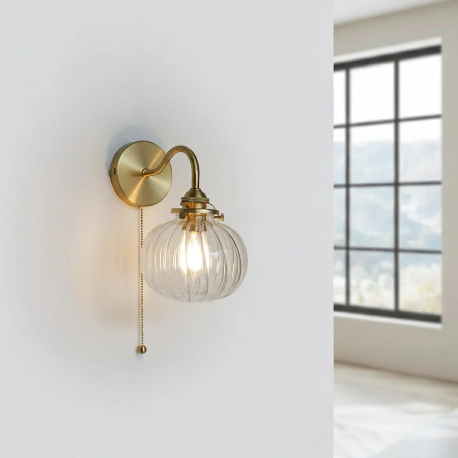 Wandleuchte mit Glaskugel und goldener Kupferoptik an weißer Wand